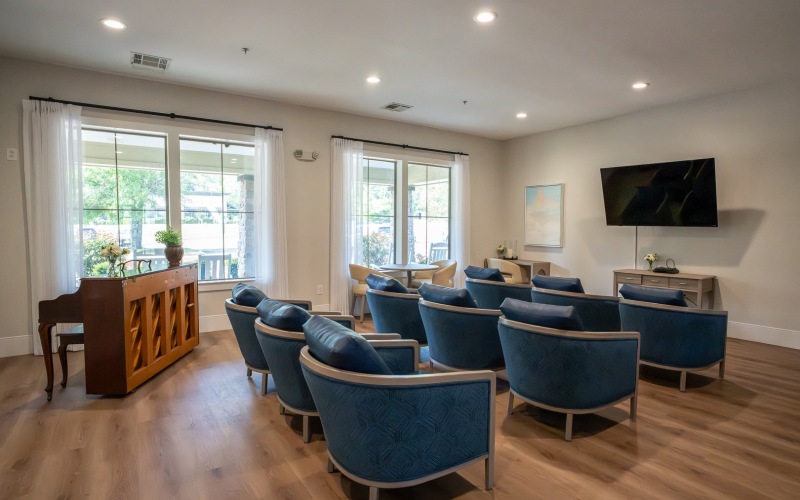 a room with a piano and rows of chairs facing a tv